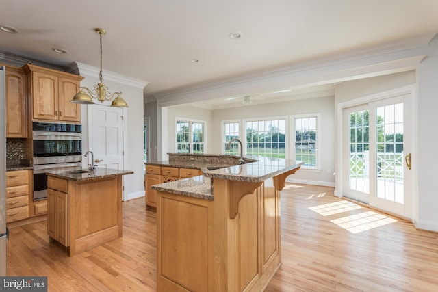 kitchen featuring hanging light fixtures, light hardwood / wood-style floors, a kitchen breakfast bar, a center island with sink, and ornamental molding