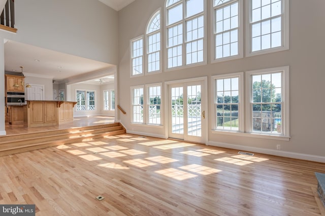 unfurnished living room with light hardwood / wood-style floors, crown molding, and a healthy amount of sunlight