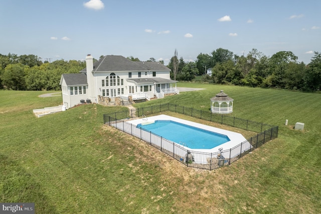 back of property with a fenced in pool and a lawn