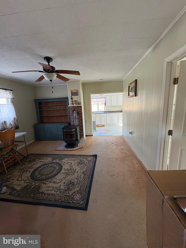 carpeted living area featuring ceiling fan, ornamental molding, a wood stove, and wooden walls