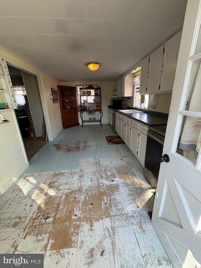 kitchen featuring light wood-type flooring, dark countertops, electric range, and a sink