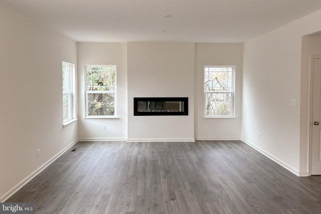 unfurnished living room with visible vents, baseboards, wood finished floors, and a glass covered fireplace