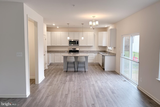 kitchen with baseboards, a kitchen island, appliances with stainless steel finishes, wood finished floors, and white cabinetry