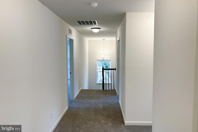 hallway featuring dark colored carpet, visible vents, and baseboards