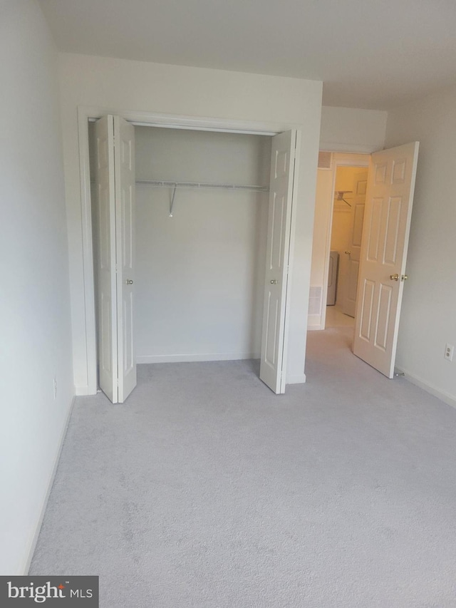 unfurnished bedroom featuring light colored carpet, a closet, and washer / clothes dryer