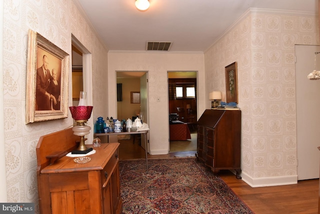 corridor featuring wood finished floors, visible vents, baseboards, ornamental molding, and wallpapered walls