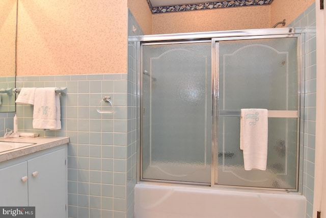 full bath with combined bath / shower with glass door, wainscoting, vanity, and tile walls