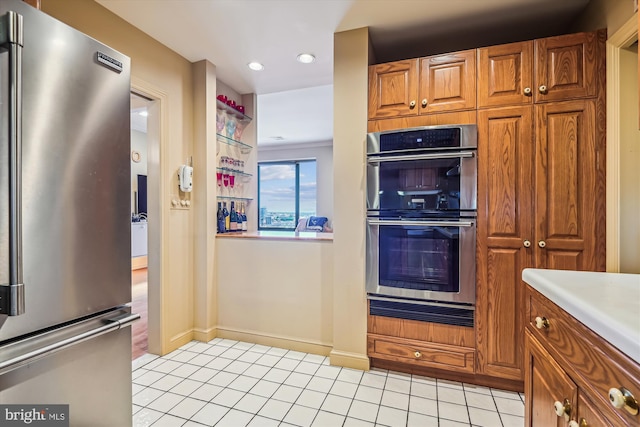 kitchen with light tile patterned floors, light countertops, appliances with stainless steel finishes, brown cabinetry, and baseboards