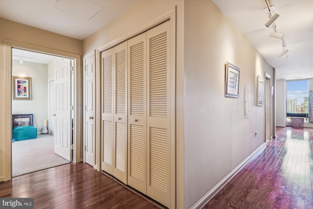 corridor featuring track lighting, baseboards, and hardwood / wood-style floors