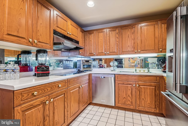 kitchen featuring light tile patterned floors, under cabinet range hood, a sink, appliances with stainless steel finishes, and brown cabinets