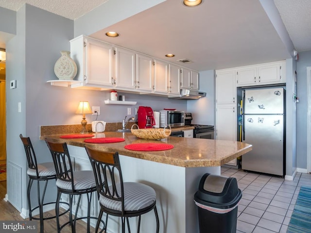 kitchen with appliances with stainless steel finishes, white cabinetry, a peninsula, and light tile patterned floors