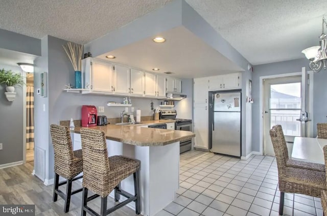 kitchen with a textured ceiling, a peninsula, appliances with stainless steel finishes, and white cabinets