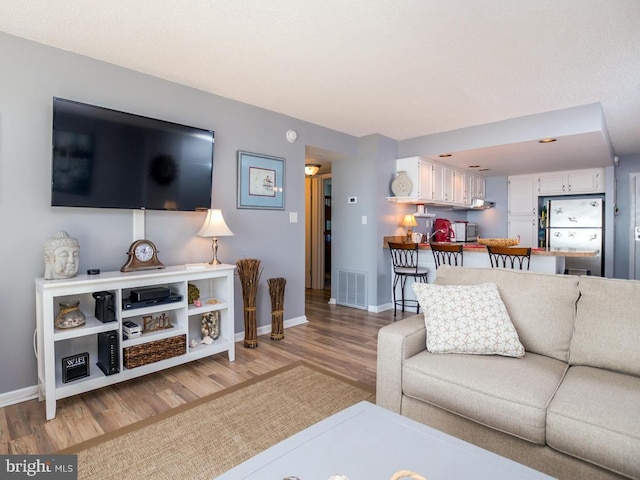 living area with light wood-style flooring, visible vents, and baseboards