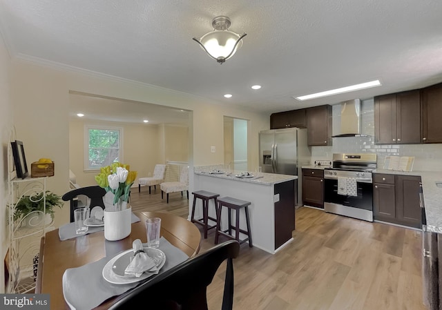 kitchen with tasteful backsplash, wall chimney range hood, appliances with stainless steel finishes, and light hardwood / wood-style floors