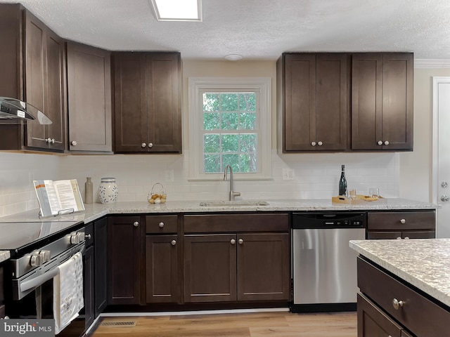 kitchen with a textured ceiling, dark brown cabinets, appliances with stainless steel finishes, light hardwood / wood-style floors, and sink