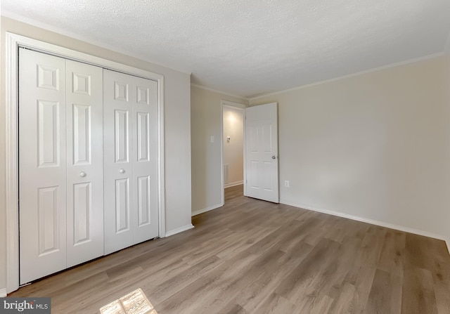 unfurnished bedroom with light wood-type flooring, a textured ceiling, ornamental molding, and a closet