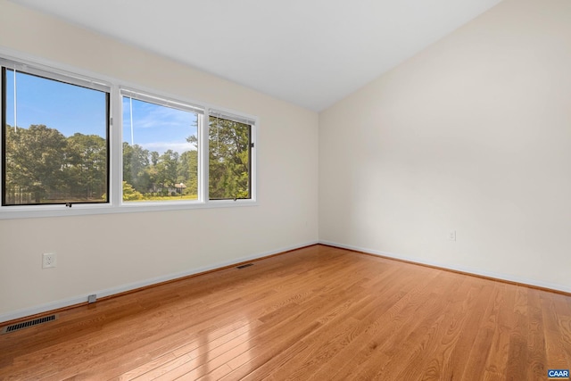 unfurnished room with light wood-style floors, baseboards, visible vents, and vaulted ceiling