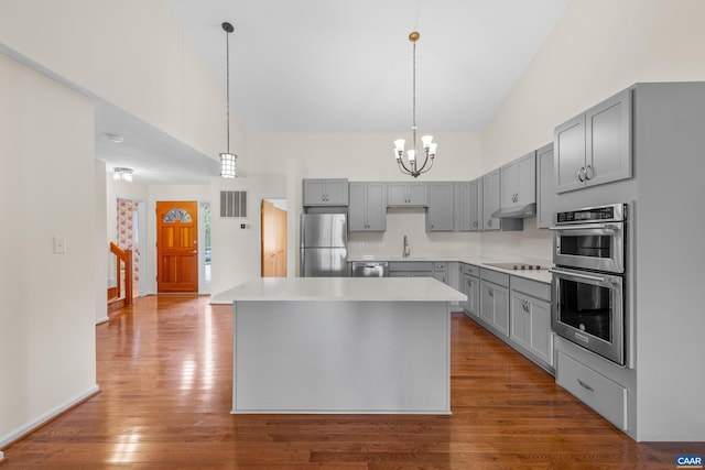 kitchen with dark wood-style floors, gray cabinets, visible vents, a towering ceiling, and appliances with stainless steel finishes