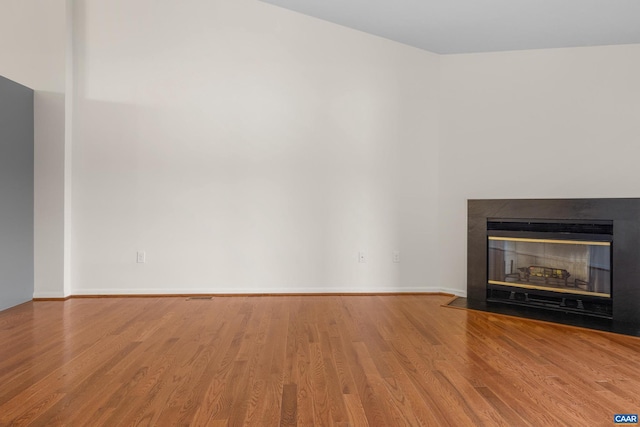 unfurnished living room featuring a fireplace with flush hearth, baseboards, and wood finished floors