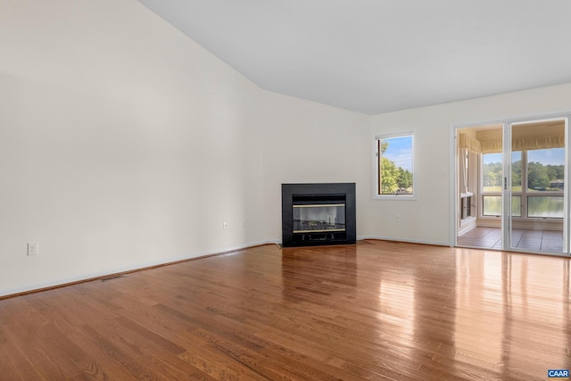 unfurnished living room with baseboards, a fireplace with flush hearth, visible vents, and wood finished floors