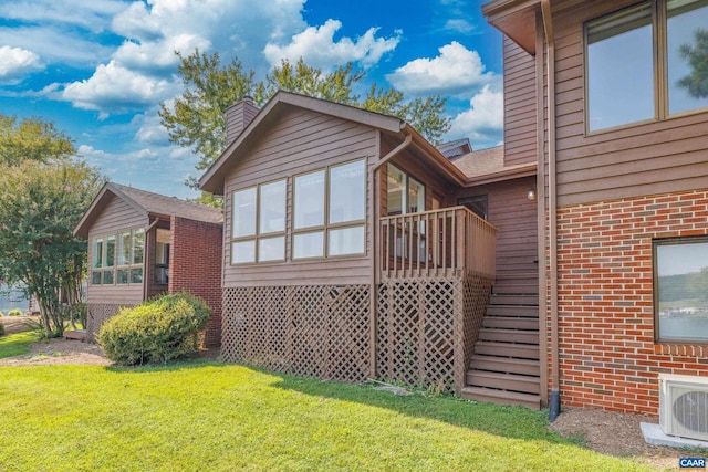 rear view of property featuring brick siding, a sunroom, stairs, a yard, and ac unit