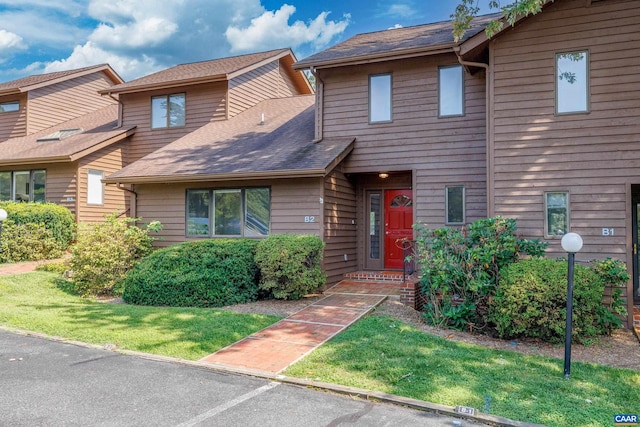 townhome / multi-family property featuring roof with shingles and a front lawn