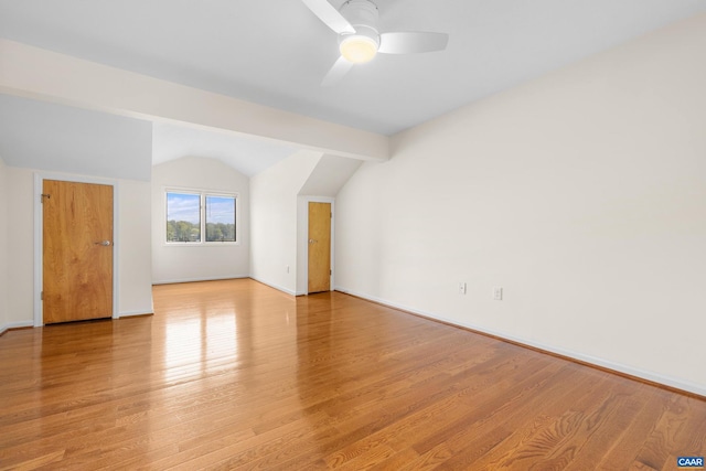 additional living space featuring vaulted ceiling with beams, light wood-style flooring, baseboards, and a ceiling fan