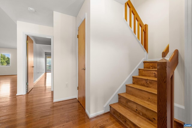 staircase featuring baseboards, wood finished floors, and a healthy amount of sunlight