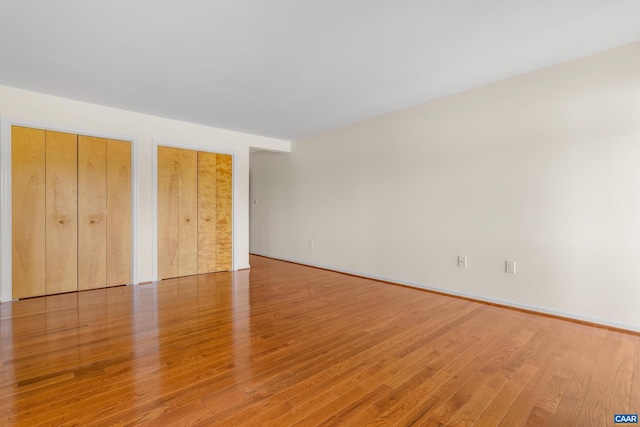 unfurnished bedroom with light wood-type flooring, two closets, and baseboards