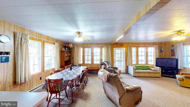 carpeted dining area with ceiling fan, baseboard heating, plenty of natural light, and wooden walls