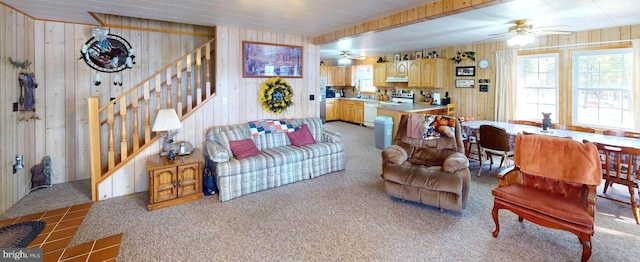 living room with wooden walls, light colored carpet, ceiling fan, and stairway