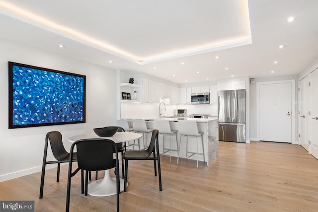 dining area with recessed lighting, light wood finished floors, and a raised ceiling