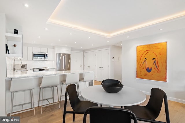 dining room with light wood-style floors, recessed lighting, and a raised ceiling