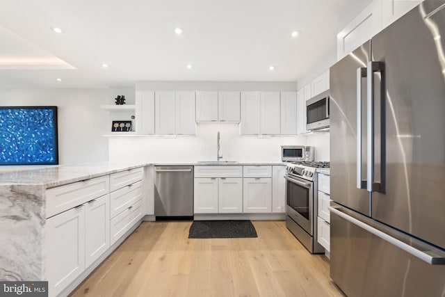 kitchen with appliances with stainless steel finishes, a sink, open shelves, white cabinetry, and light wood finished floors