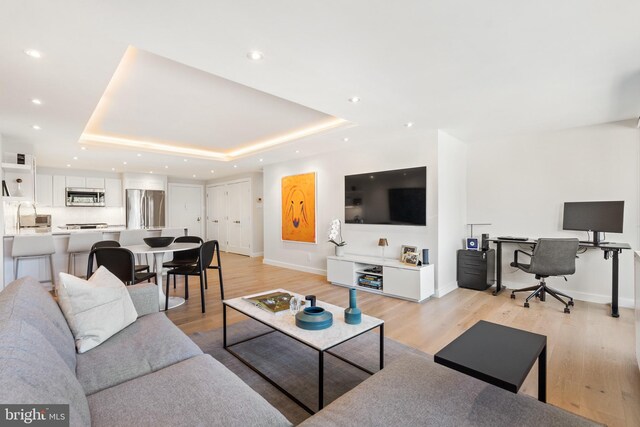 living room with light wood-style floors, baseboards, a raised ceiling, a desk, and recessed lighting