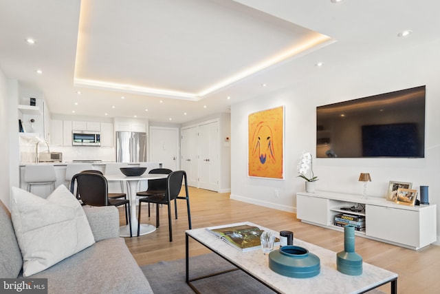 living area featuring a raised ceiling, light wood-style flooring, recessed lighting, and baseboards