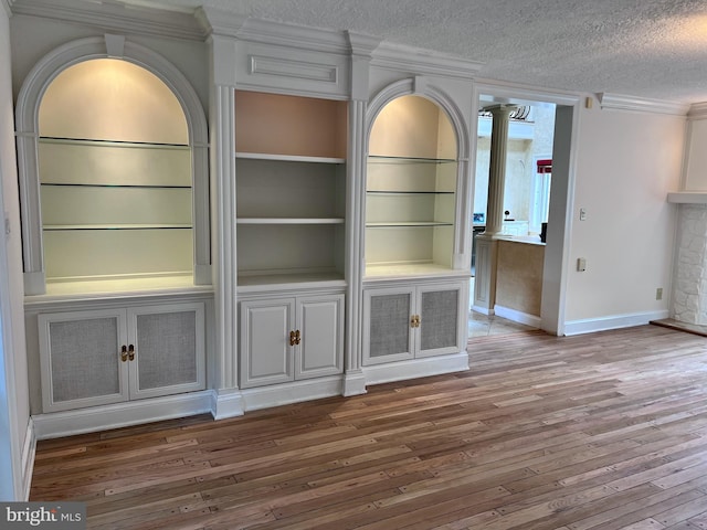 unfurnished living room featuring a textured ceiling, wood-type flooring, decorative columns, and crown molding