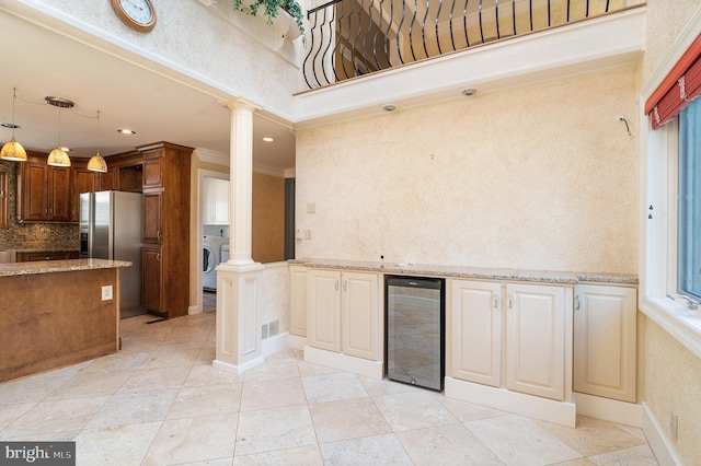 kitchen featuring wine cooler, washer / dryer, decorative columns, crown molding, and stainless steel fridge