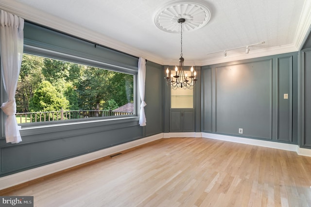 spare room featuring rail lighting, a notable chandelier, light hardwood / wood-style flooring, and a healthy amount of sunlight