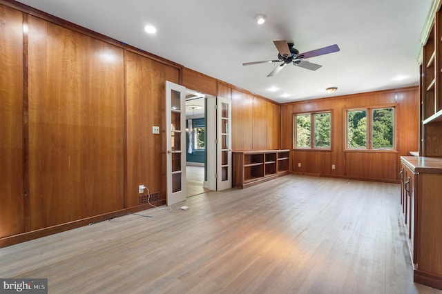 unfurnished living room featuring light wood-type flooring, ornamental molding, wooden walls, and ceiling fan