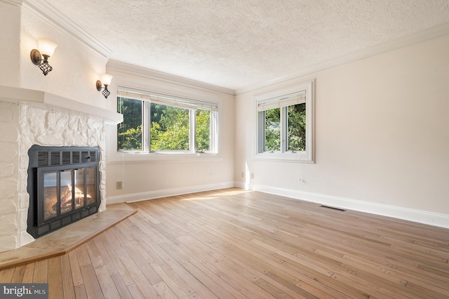 unfurnished living room with light wood-type flooring, a textured ceiling, a stone fireplace, and crown molding