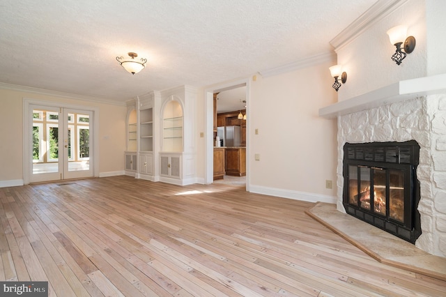 unfurnished living room featuring a stone fireplace, a textured ceiling, crown molding, light hardwood / wood-style flooring, and built in shelves