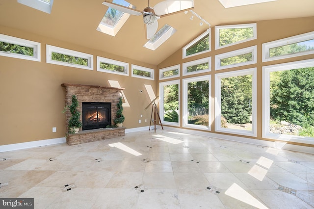 unfurnished living room featuring a fireplace, ceiling fan, a skylight, and high vaulted ceiling