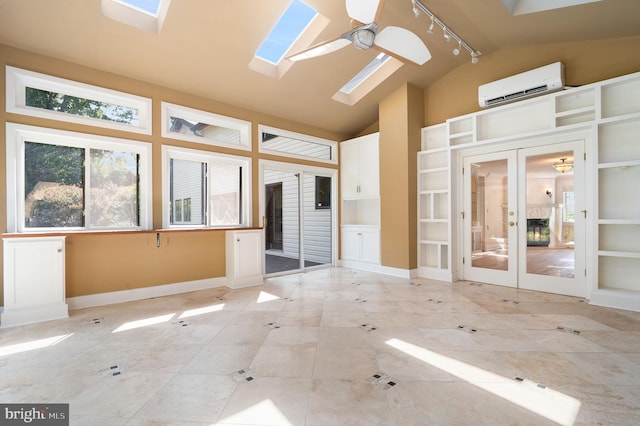 unfurnished sunroom featuring vaulted ceiling with skylight, rail lighting, a wall mounted air conditioner, ceiling fan, and french doors