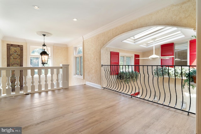 hallway with wood-type flooring, a skylight, a raised ceiling, and ornamental molding