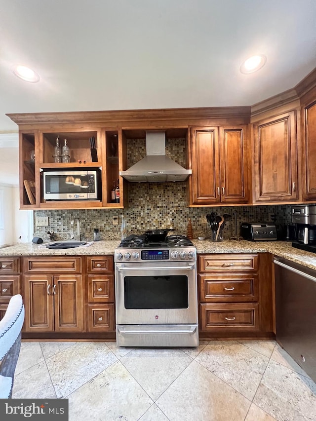 kitchen featuring appliances with stainless steel finishes, light stone counters, backsplash, sink, and wall chimney range hood