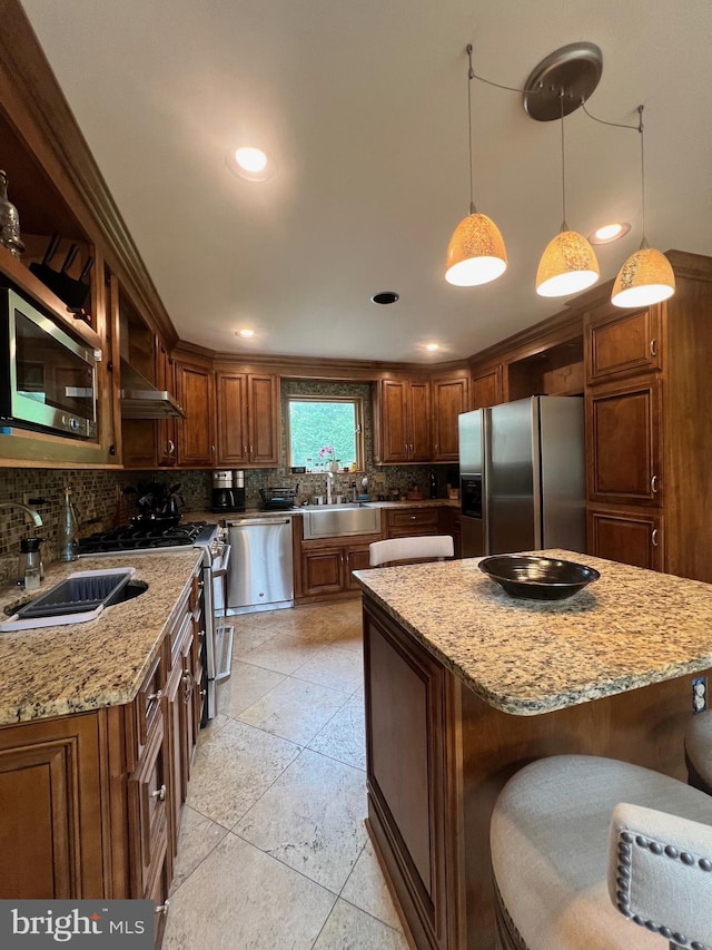 kitchen featuring light stone counters, hanging light fixtures, appliances with stainless steel finishes, a center island, and decorative backsplash