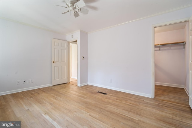 unfurnished bedroom featuring a spacious closet, ornamental molding, ceiling fan, and light hardwood / wood-style flooring