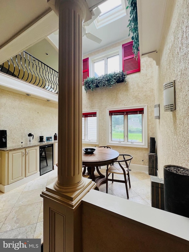 interior space with a skylight, beverage cooler, cream cabinetry, decorative columns, and crown molding