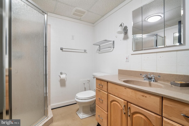 bathroom with a paneled ceiling, vanity, toilet, and a shower with door